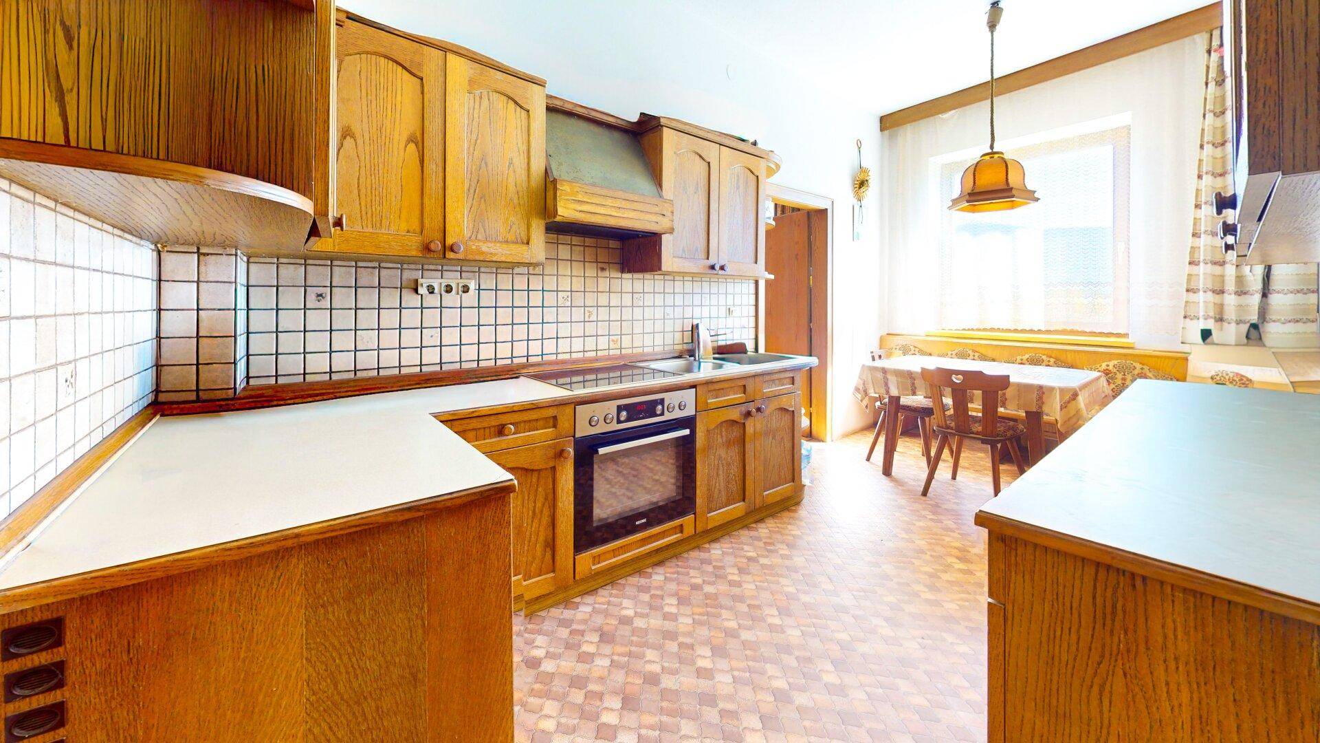 Helle, traditionelle Küche mit Holzschränken, Fliesenrückwand und Essbereich am Fenster.