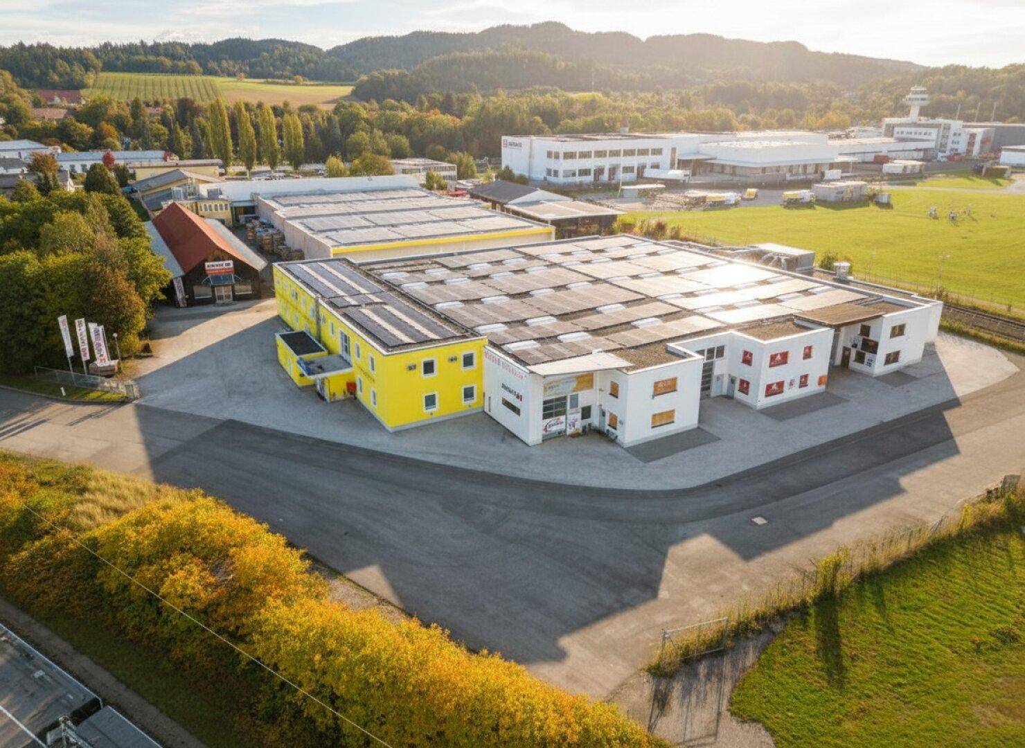 Luftaufnahme eines modernen Gewerbeparks mit mehreren Gebäuden und Solaranlagen auf den Dächern.