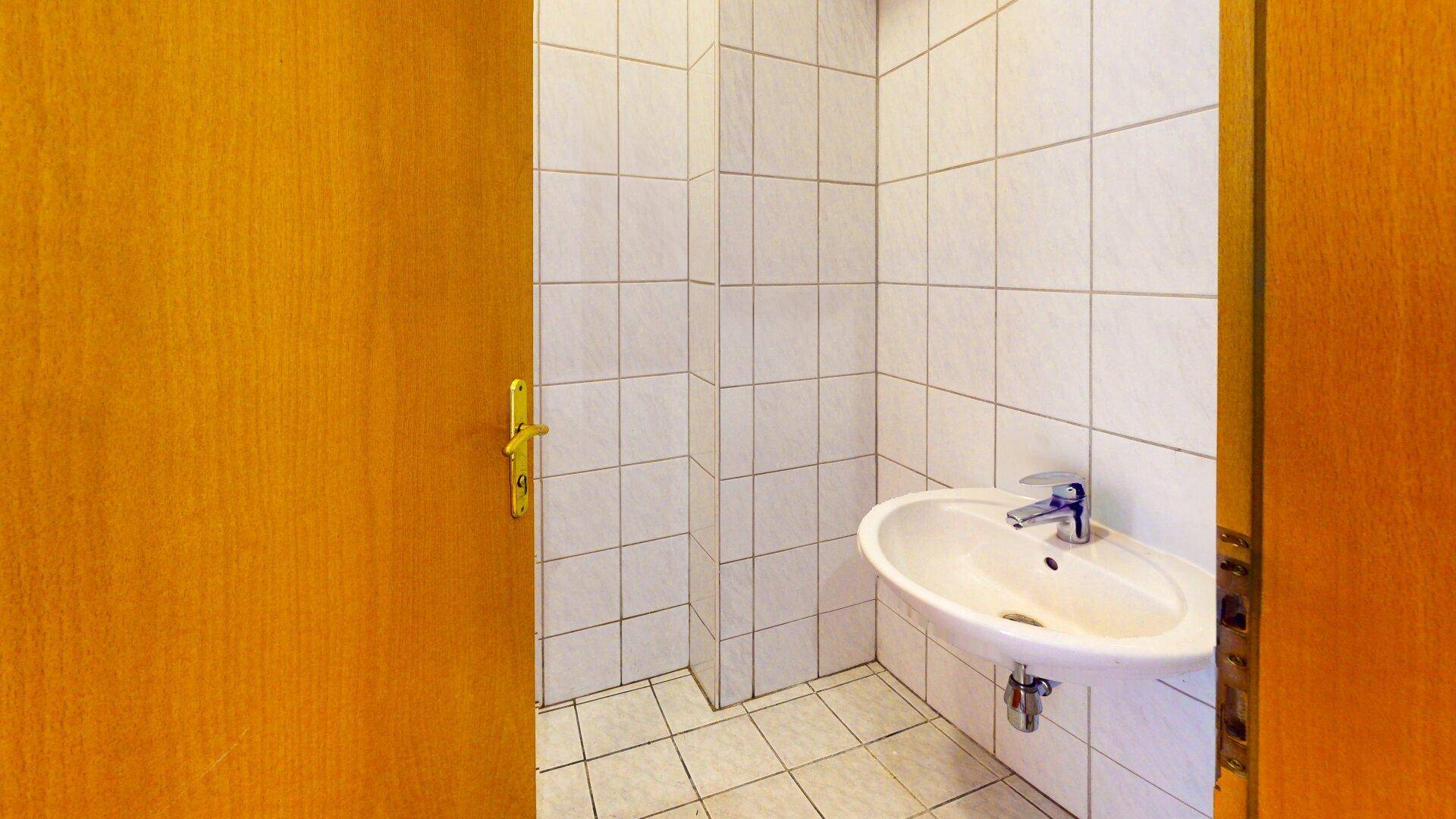 Kleines Badezimmer mit weißem Waschbecken, Fliesen an Wänden und Boden, umgeben von Holztüren.