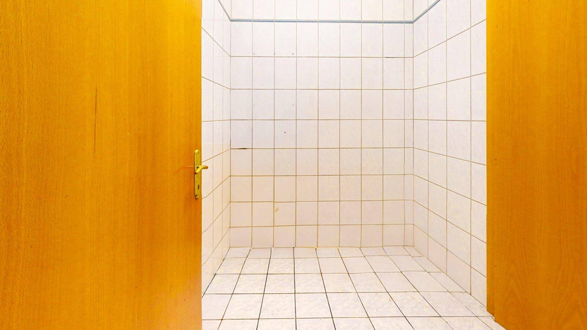 Einfacher Duschbereich mit weißen Fliesen an Wänden und Boden, umgeben von Holztüren.