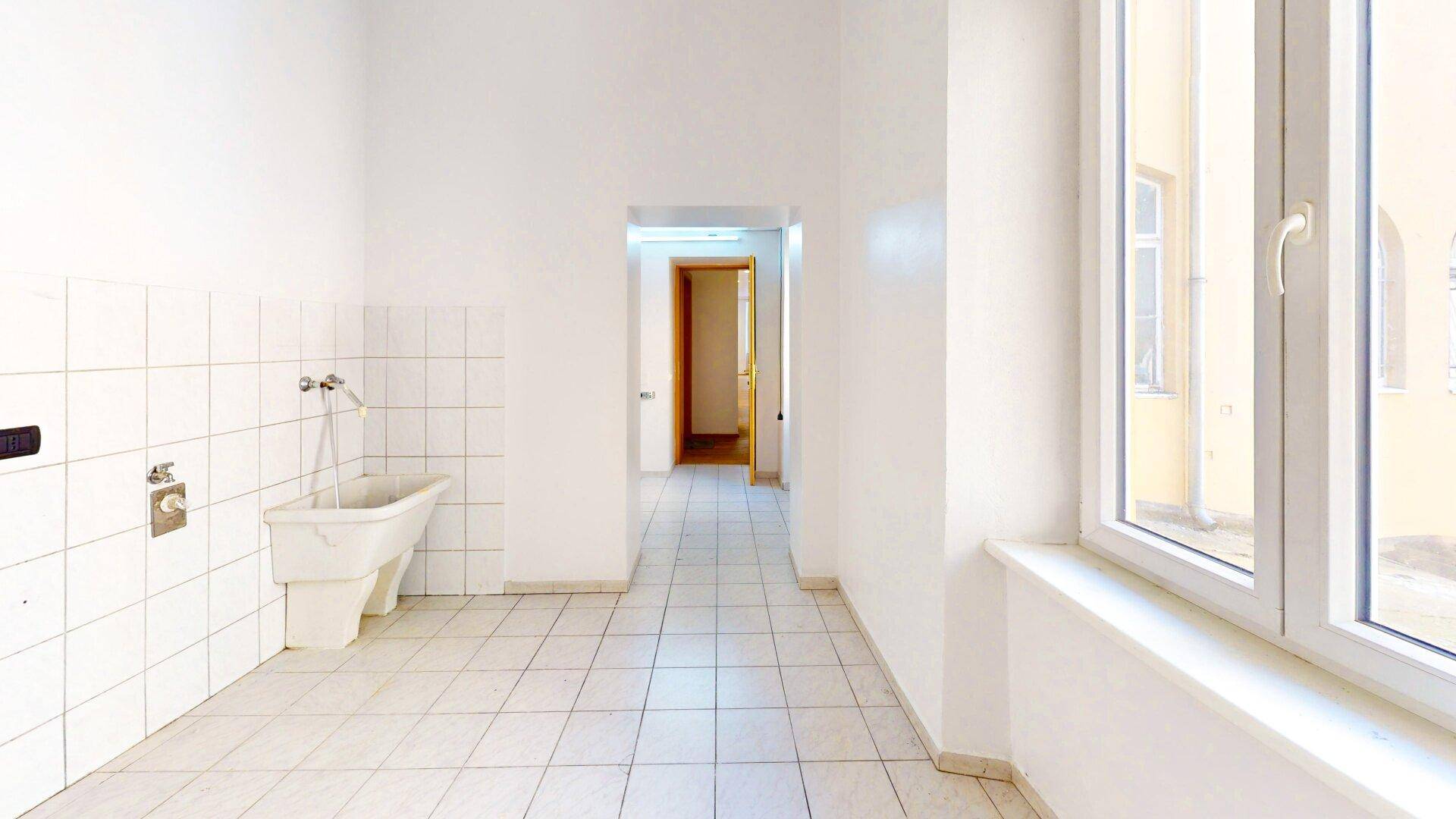 Geräumiger Hauswirtschaftsraum mit weißen Fliesen, Waschbecken und einem großen Fenster.