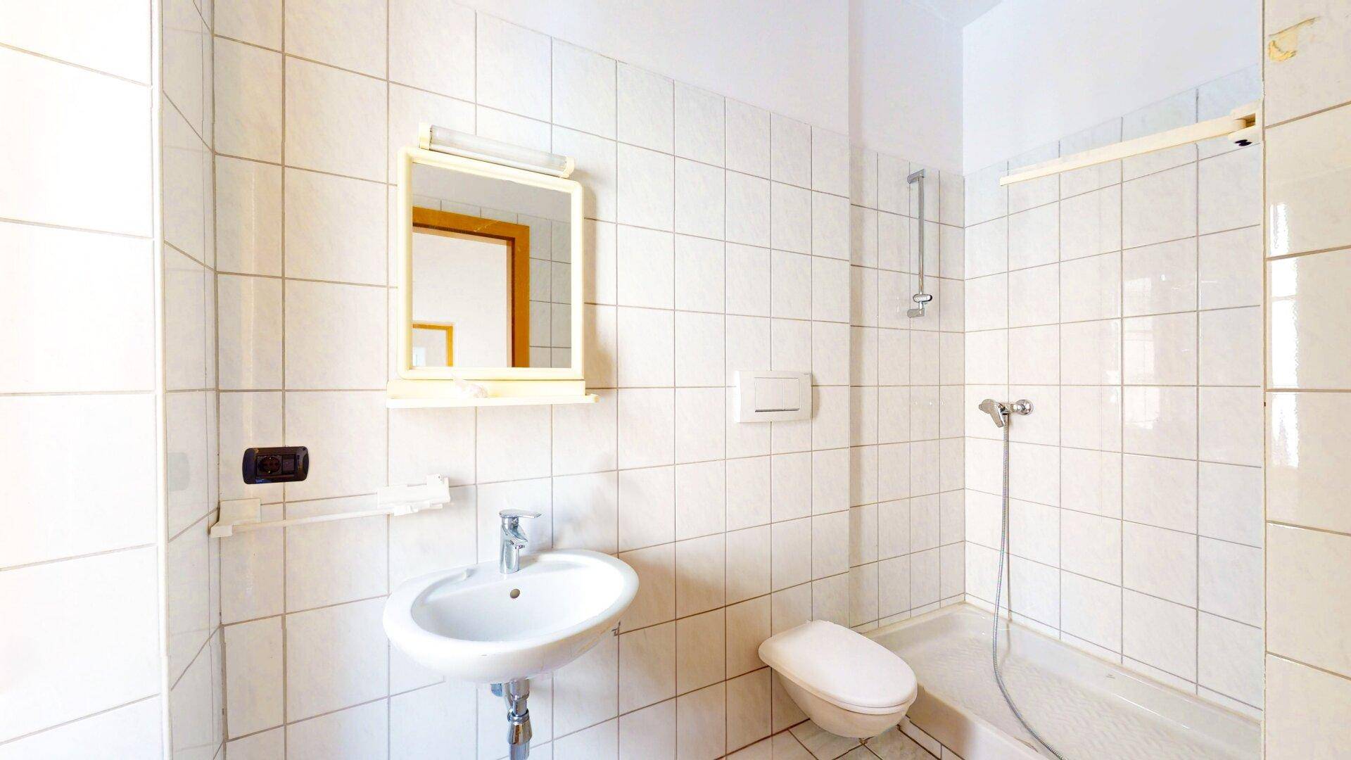 Badezimmer mit weißen Fliesen, Waschbecken, Toilette und Duschbereich.