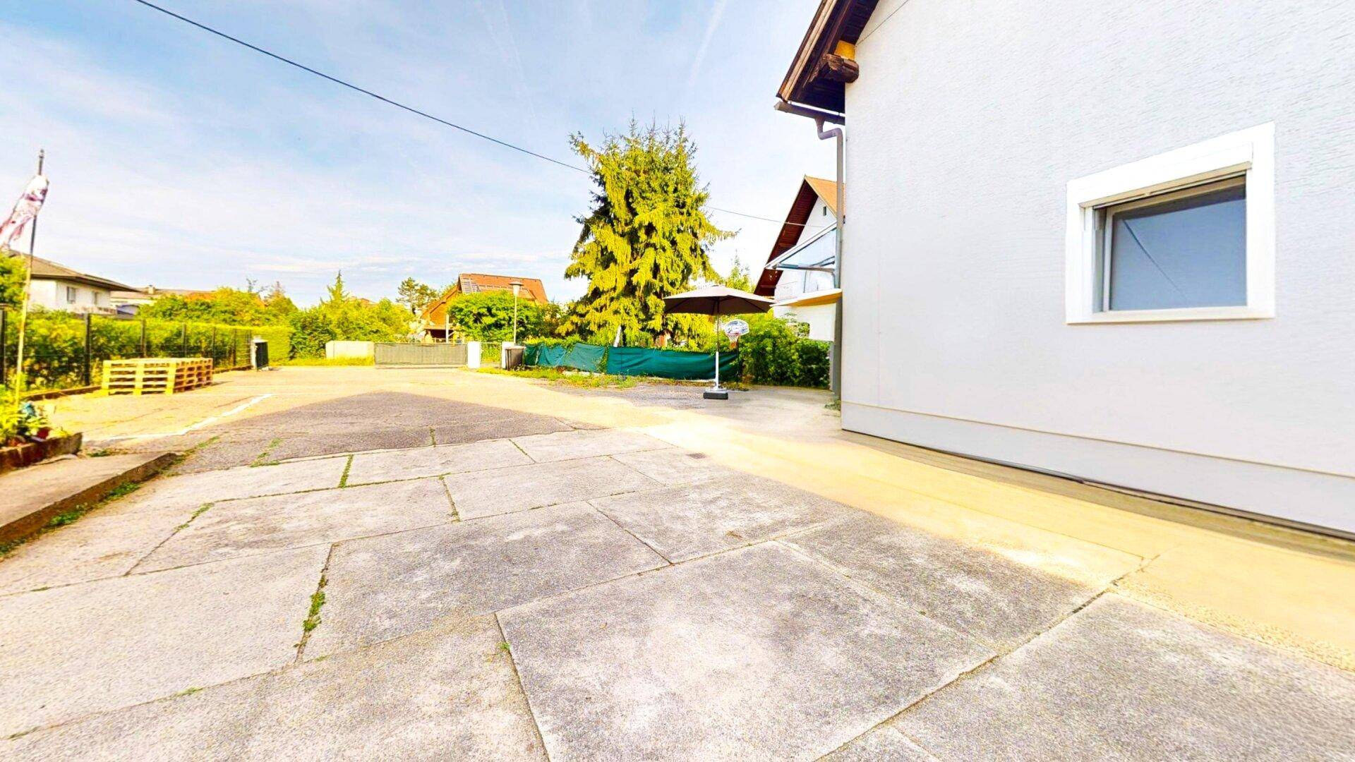 Gepflasterter Außenbereich neben dem Haus mit viel Platz und einem Sonnenschirm.