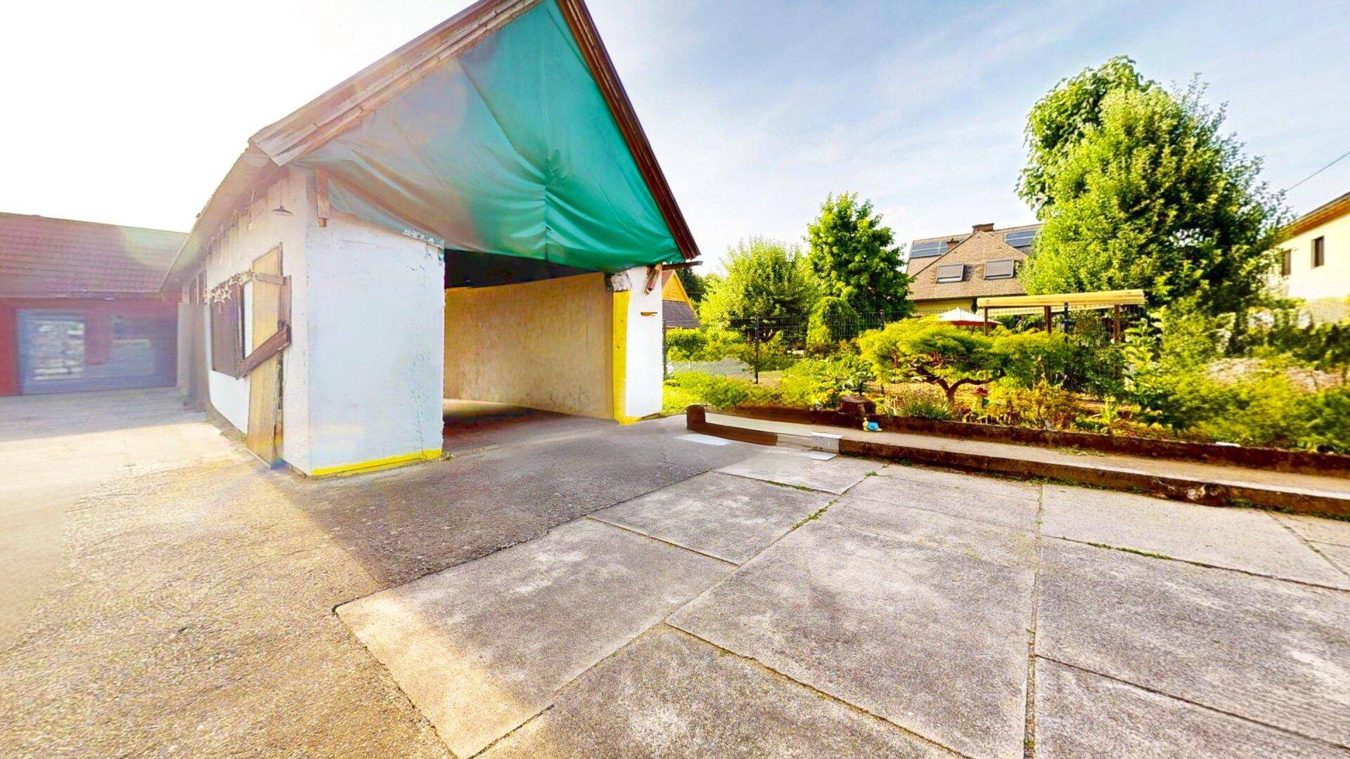 Offene Garage oder Carport mit Betonboden und einem provisorischen Dach.