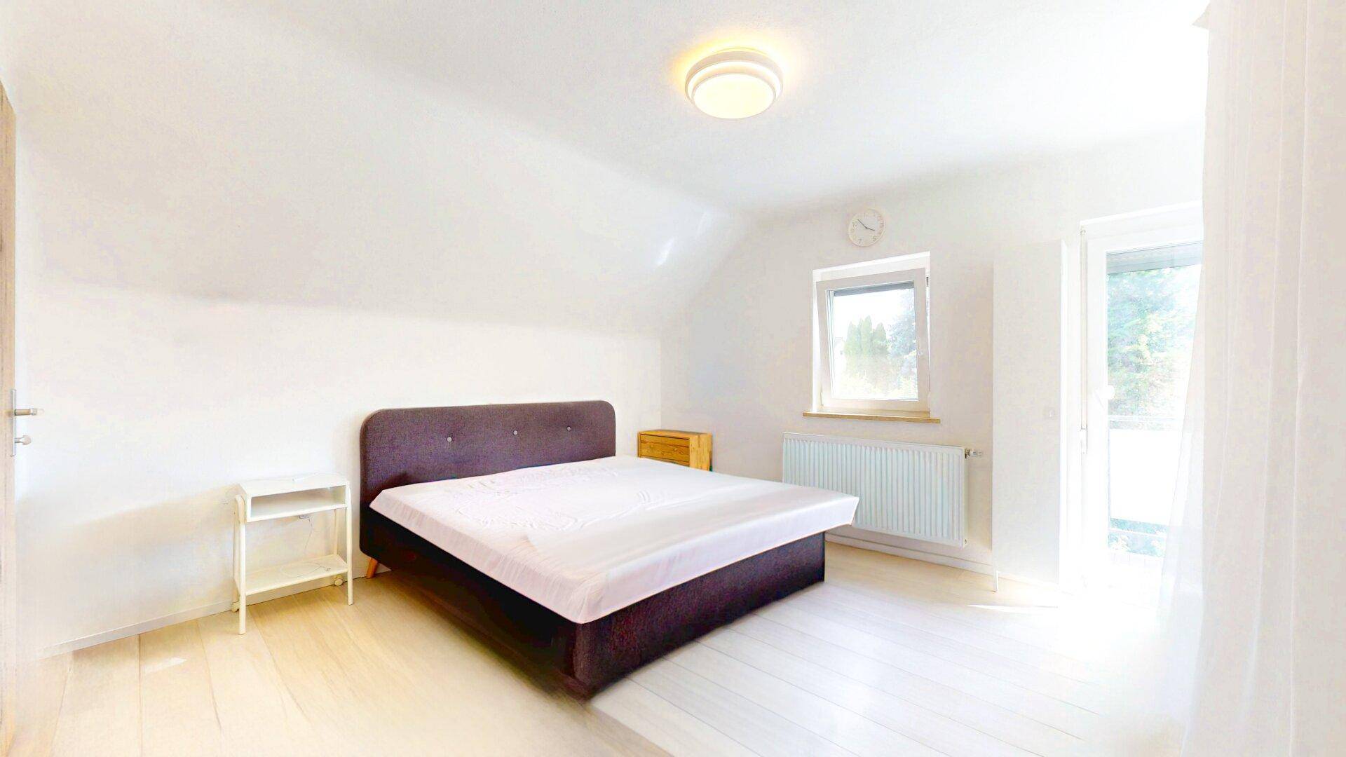 Helles Schlafzimmer im Dachgeschoss mit schrägen Wänden, Doppelbett und Zugang zum Balkon.
