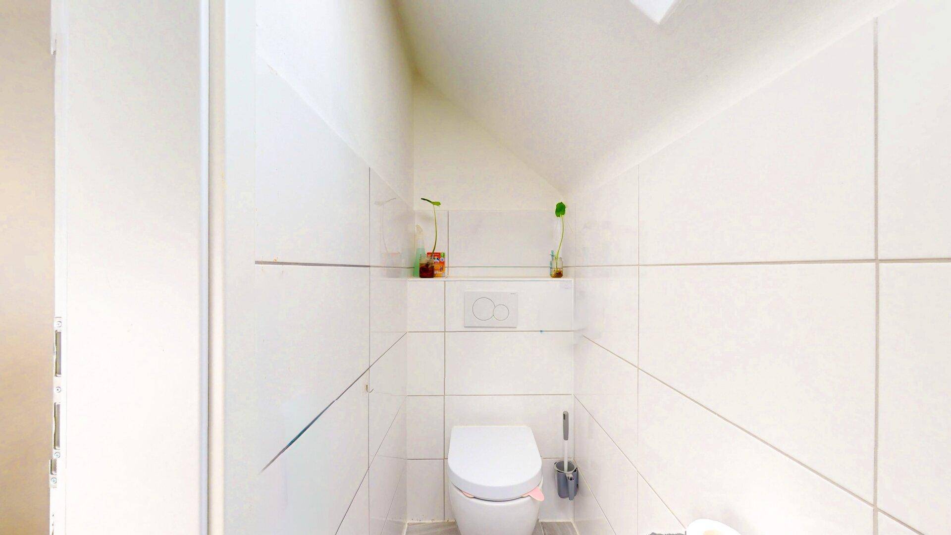 Modern gefliestes Gäste-WC mit wandhängendem WC und minimalistischem Design.