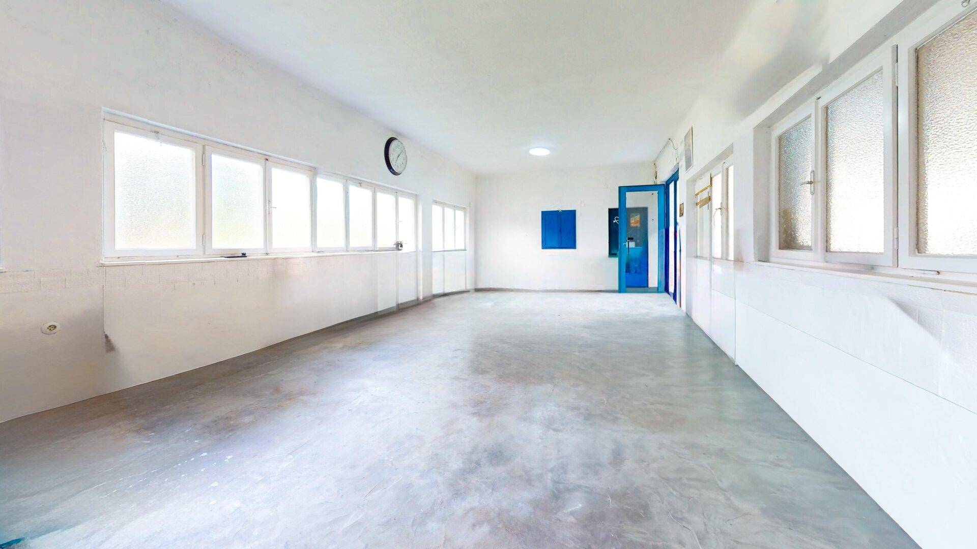 Großer, heller Raum mit vielen Fenstern und Betonboden, vielseitig nutzbar.