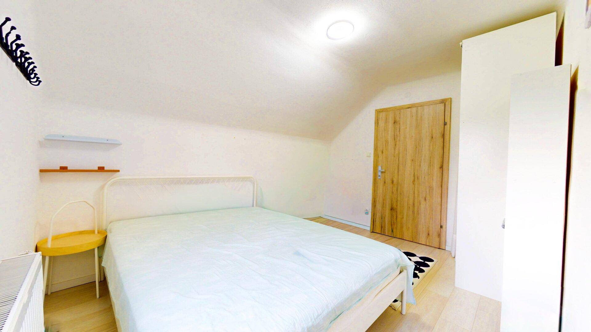 Schlafzimmer mit hellem Holzboden, weißem Bett und Kleiderschrank im Dachgeschoss.