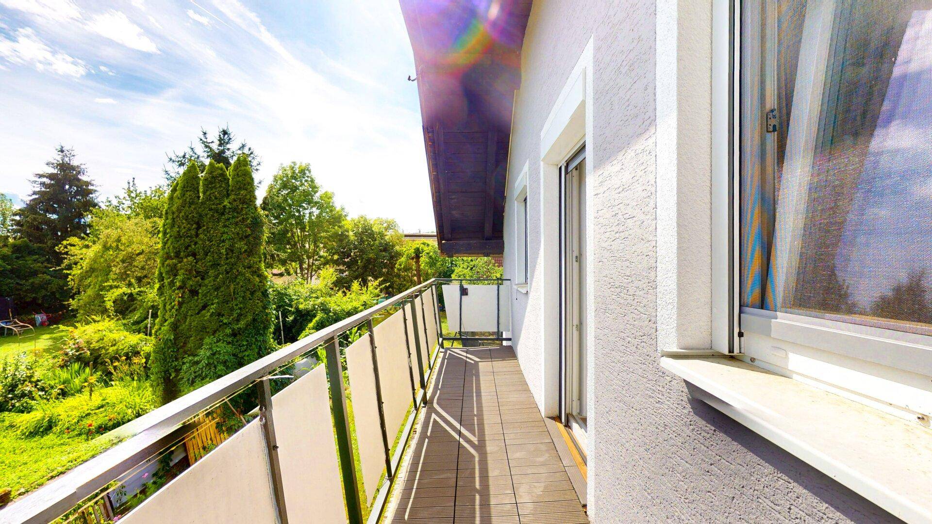 Langer Balkon mit Holzboden und Metallgeländer, bietet einen weiten Blick ins Grüne.