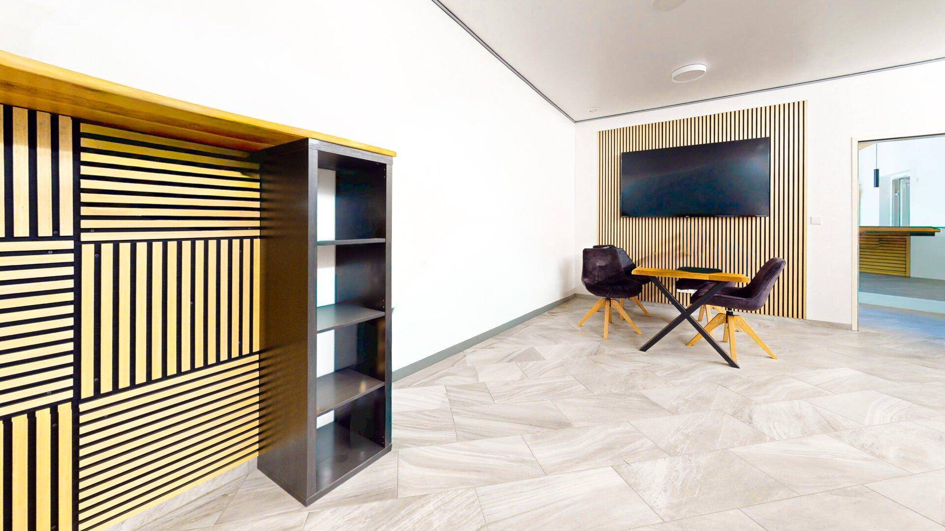 Gemütlicher Loungebereich mit Holzlamellenwand, Fliesenboden und modernen Sitzgelegenheiten für Besucher.