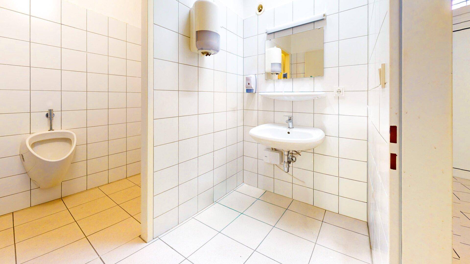 Gefliestes Badezimmer mit Urinal, Waschbecken und einem Spender für Handtücher, sehr funktional.