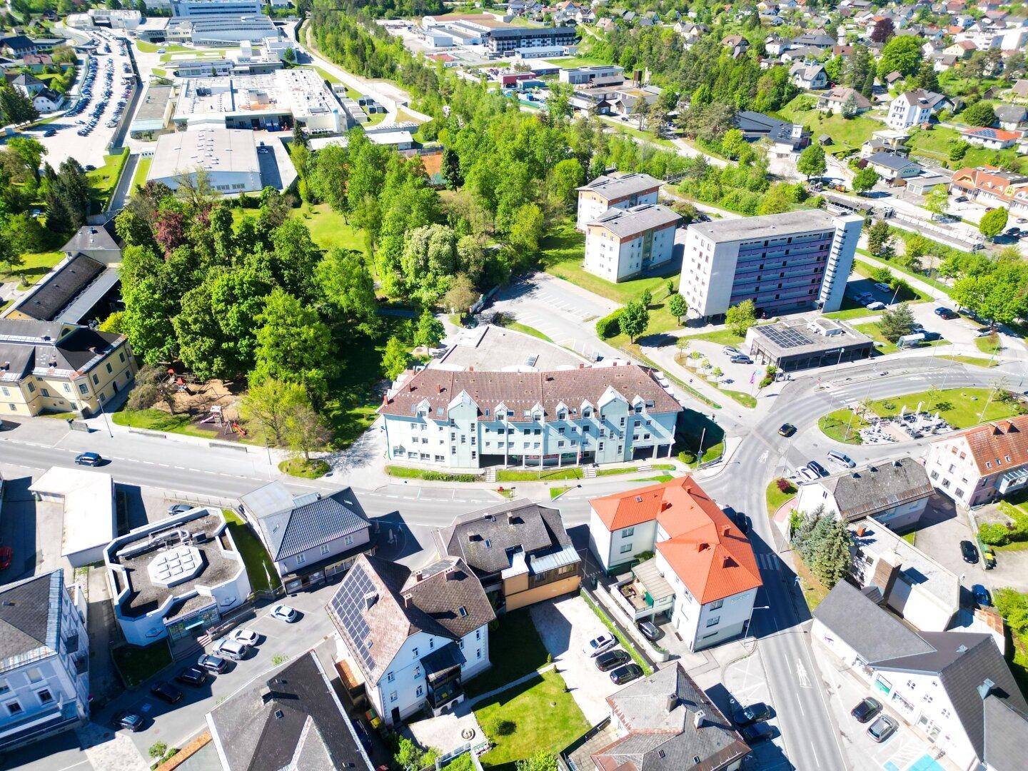 Weitläufige Luftaufnahme der Umgebung mit Wohn- und Geschäftsgebäuden sowie viel Grünfläche.