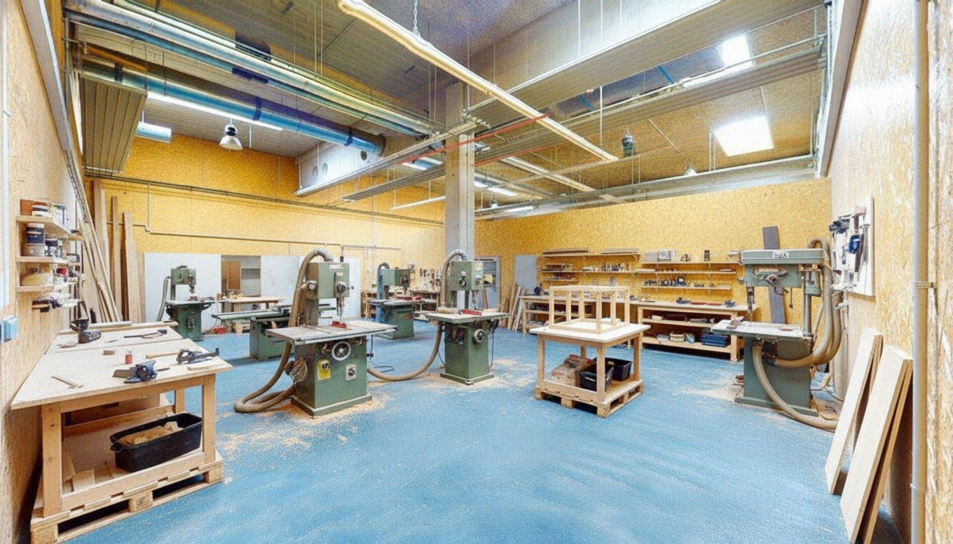 Voll ausgestattete Holzwerkstatt mit verschiedenen Maschinen, Werkbänken und viel natürlichem Licht.