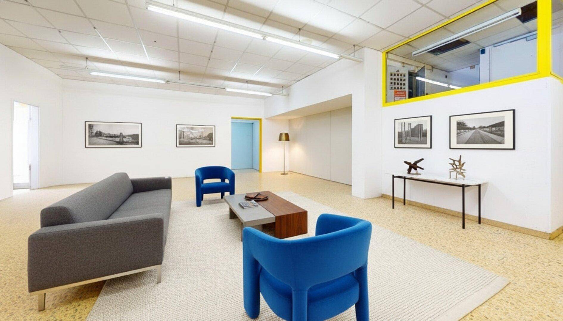 Gemütlicher Loungebereich mit modernen blauen Sesseln, einem grauen Sofa und Kunstwerken an den weißen Wänden.