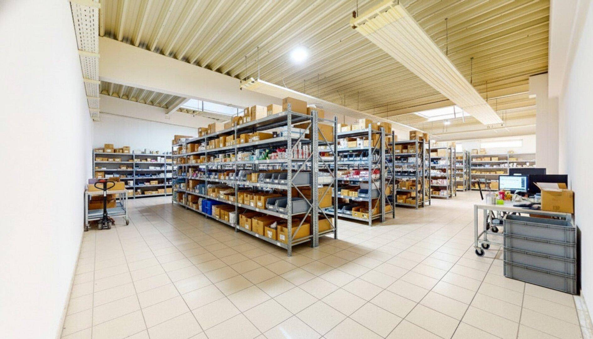 Weitläufiger Lagerbereich mit Reihen von Regalen, einem Arbeitsplatz und Oberlichtern für Tageslicht.