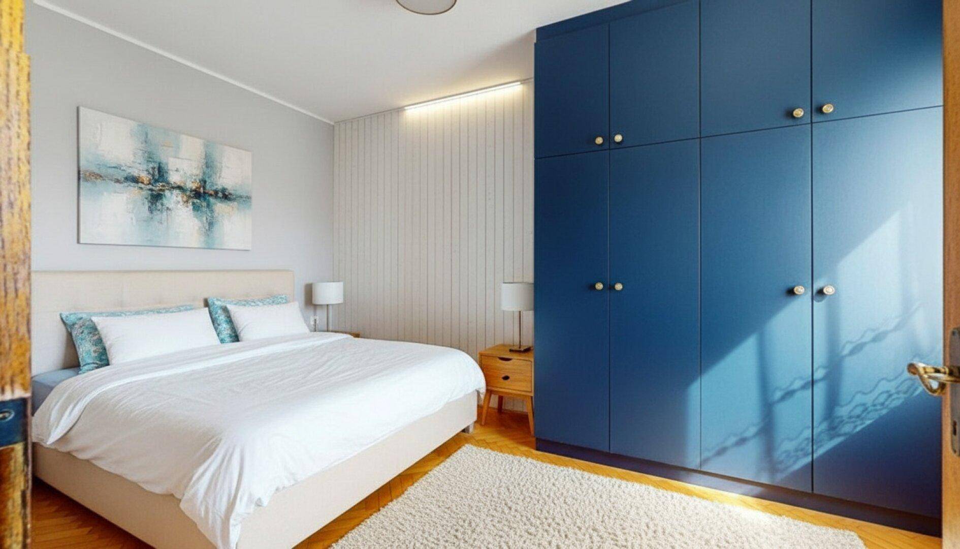 Helles Schlafzimmer mit großem Bett, blauem Einbauschrank und Holzboden.