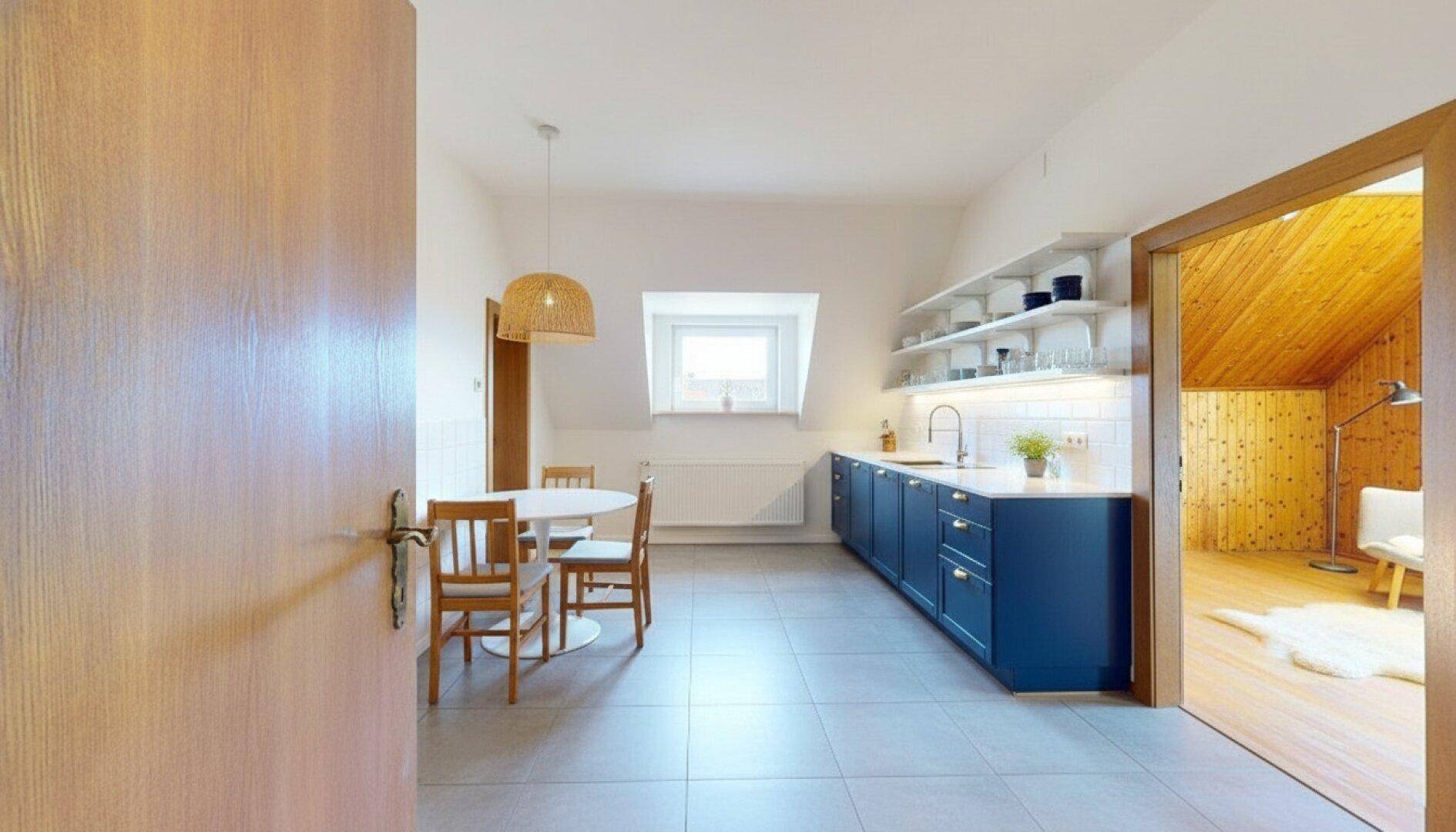 Funktionale Küche mit blauen Unterschränken, kleinem Essbereich und Blick in ein holzvertäfeltes Zimmer.