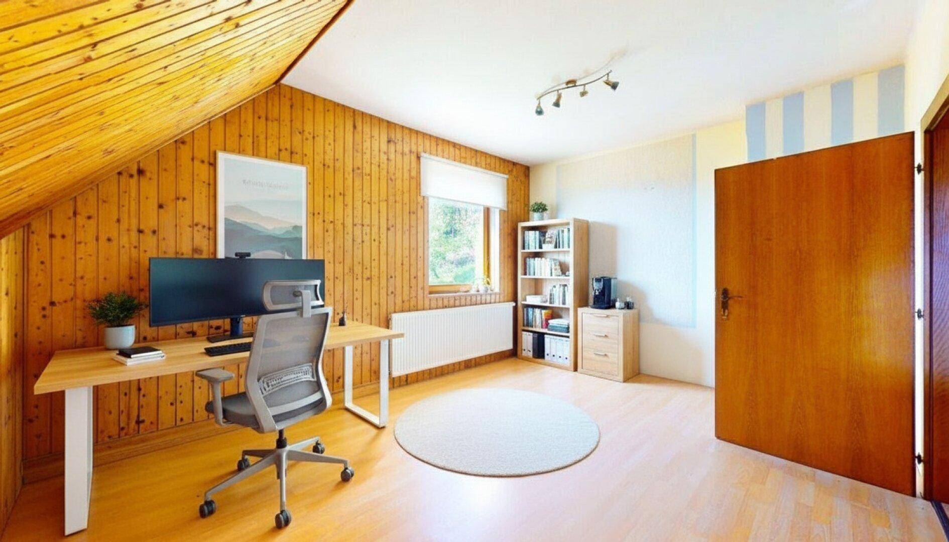 Helles Arbeitszimmer im Dachgeschoss mit Holzvertäfelung, Schreibtisch und Bücherregal.
