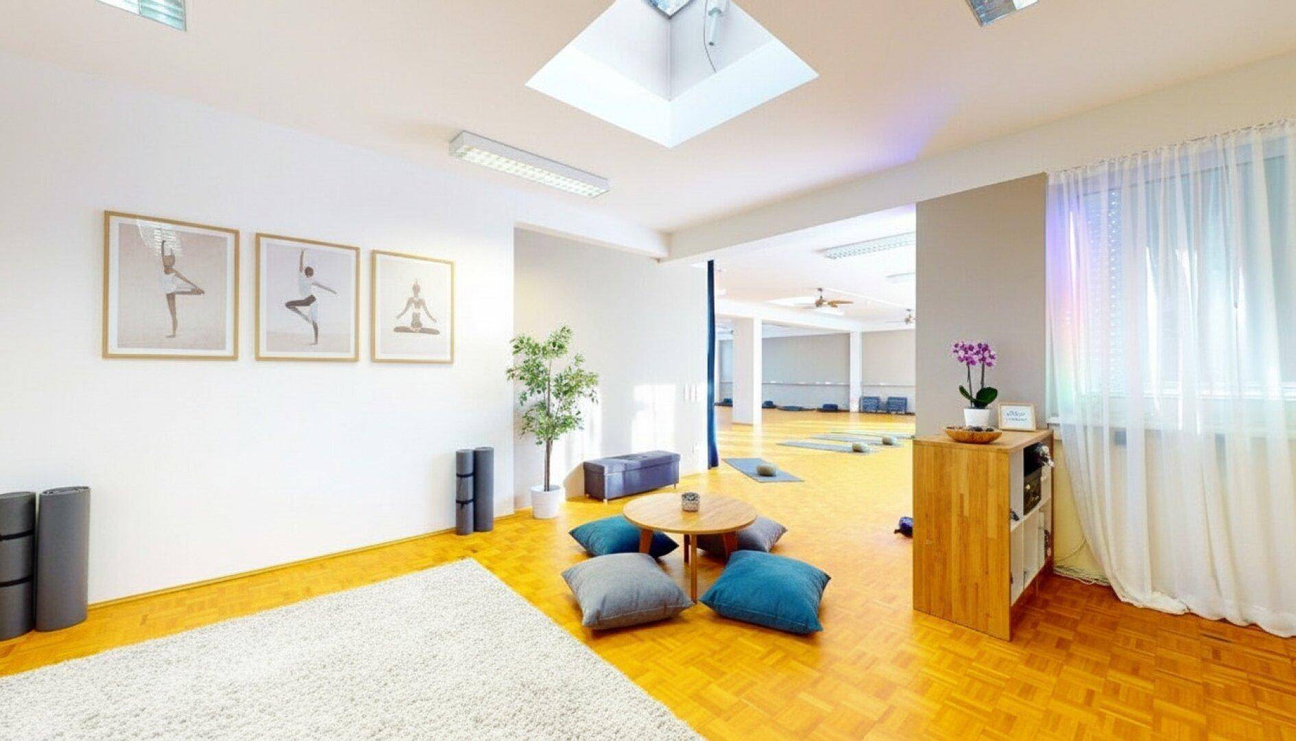 Heller und geräumiger Yogaraum mit Holzparkett, Oberlicht und gemütlicher Sitzecke für Entspannung.