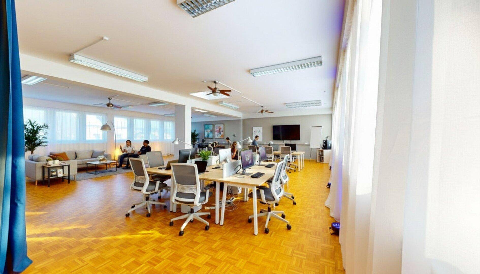 Großes, offenes Büro mit modernen Arbeitsplätzen, Lounge-Bereich und viel Tageslicht durch große Fenster.