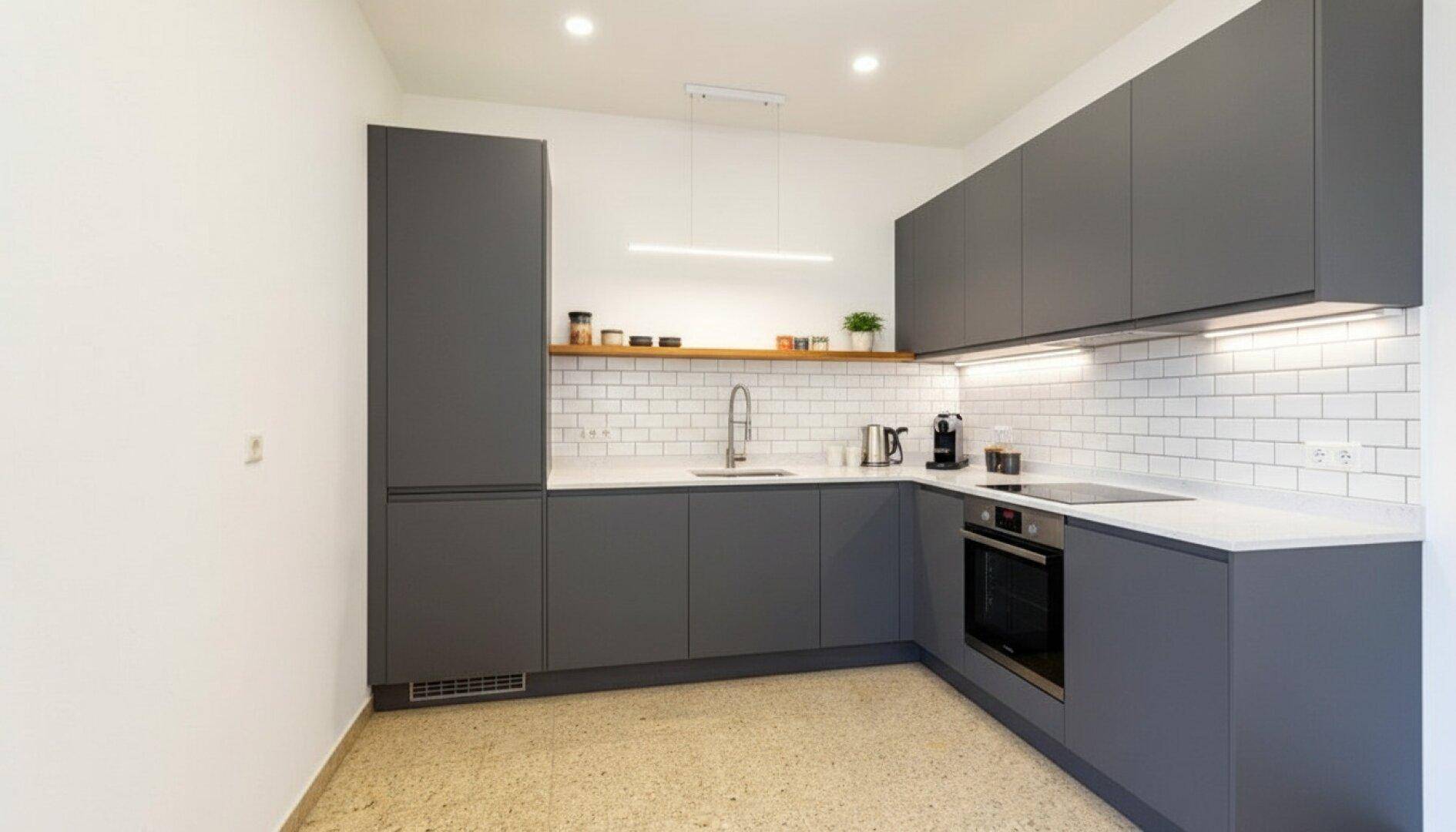 Moderne Küche mit grauen Schränken, weißem Fliesenspiegel und integrierten Geräten in minimalistischem Design.