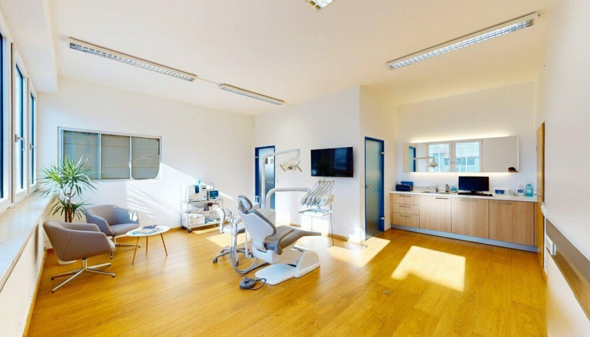 Heller Behandlungsraum mit zahnmedizinischer Ausstattung, Wartebereich und großen Fenstern.