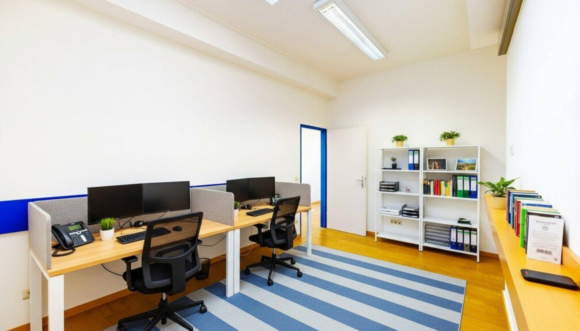 Offener Bürobereich mit mehreren Arbeitsplätzen, Schreibtischen und einem Bücherregal.