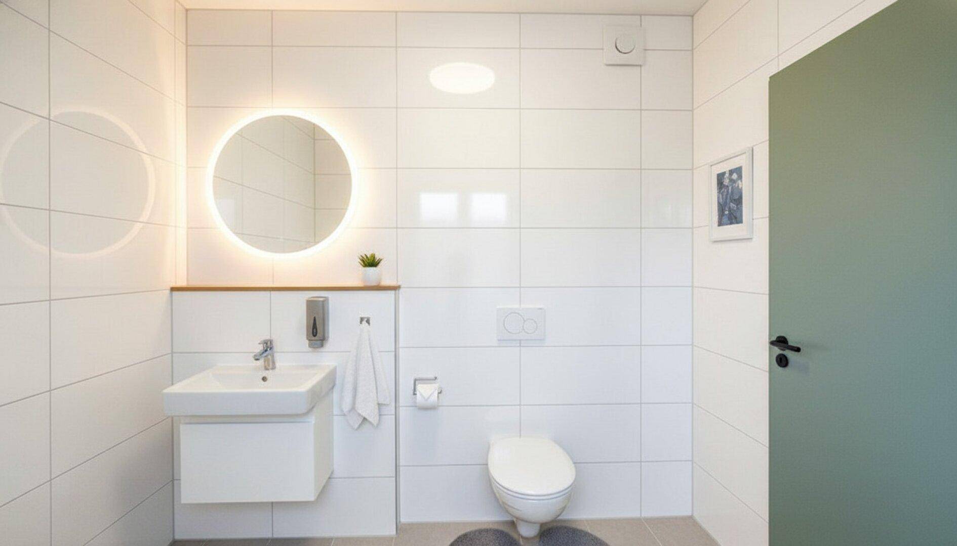 Modernes WC mit weißen Fliesen, beleuchtetem Spiegel und wandhängendem Waschbecken.