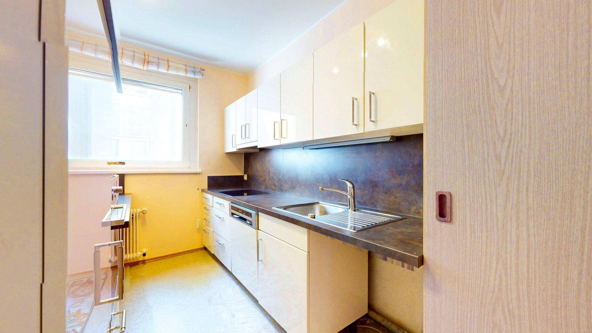 Funktionale Küche mit hellen Hochglanzschränken, Spülbecken und Fenster für Tageslicht.