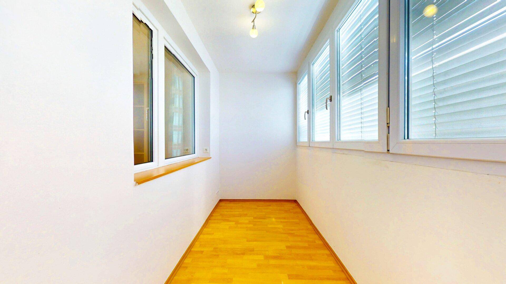 Helle Loggia mit Holzboden und großen Fenstern, ideal als zusätzlicher, lichtdurchfluteter Wohnraum.