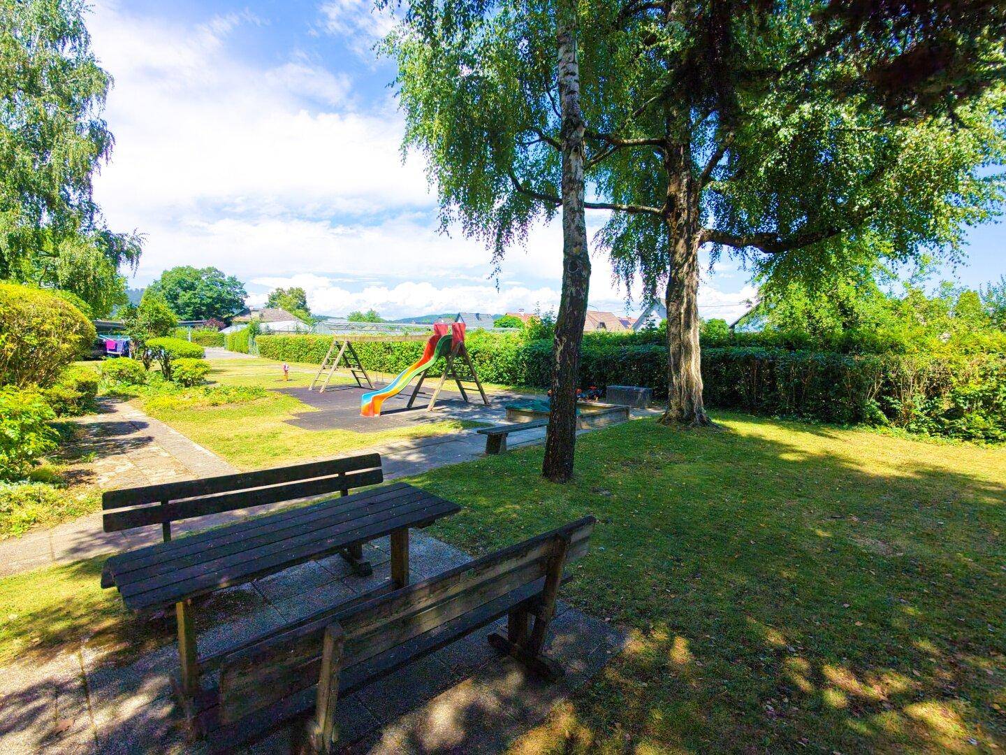 Gemeinschaftlicher Gartenbereich mit Spielplatz, Bänken und viel Grünfläche für Kinder und Erwachsene.