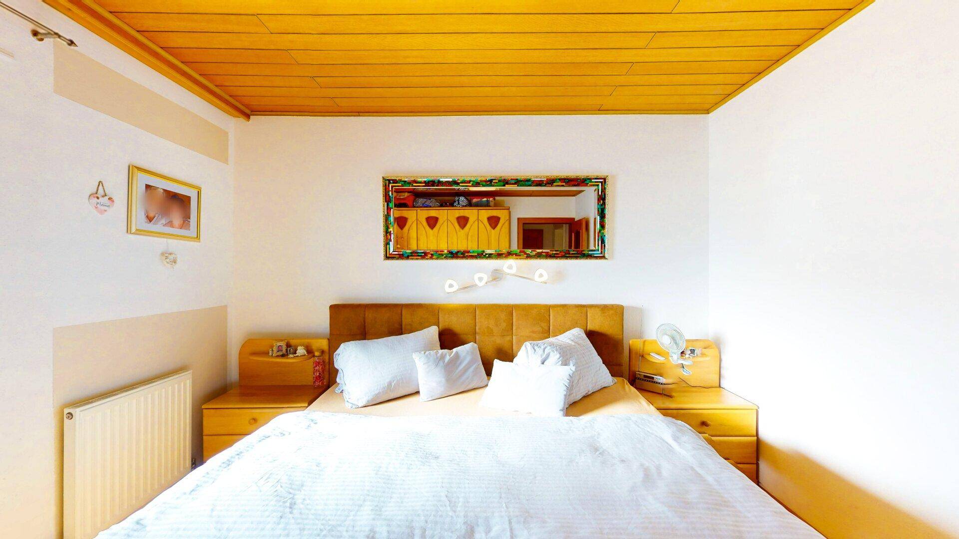 Helles Schlafzimmer mit Holzdecke, großem Bett und Nachttischen in warmen Farbtönen.