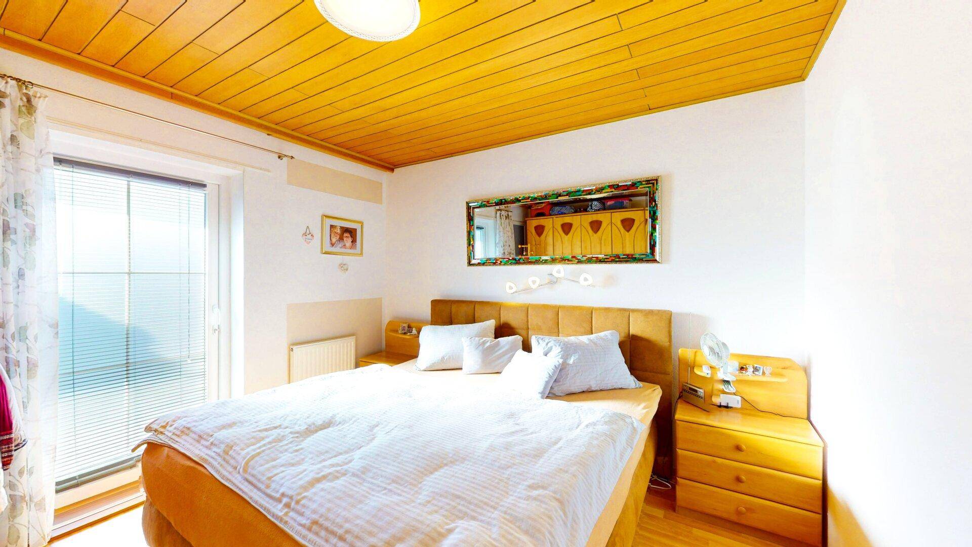 Gemütliches Schlafzimmer mit Holzdecke, Doppelbett und Zugang zu einem Balkon.