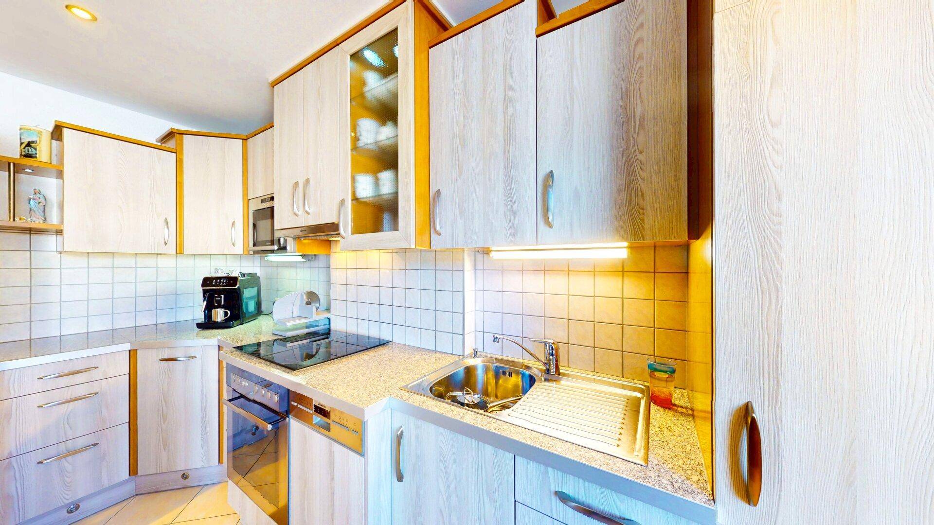 Funktionale Küche mit hellen Holzschränken, Fliesenboden und modernen Einbaugeräten.