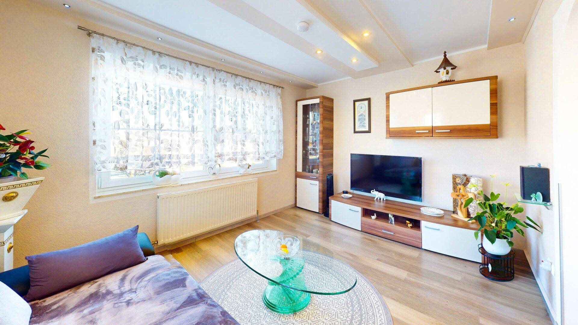Wohnzimmer mit großem Fenster, Laminatboden und moderner TV-Möbelwand.