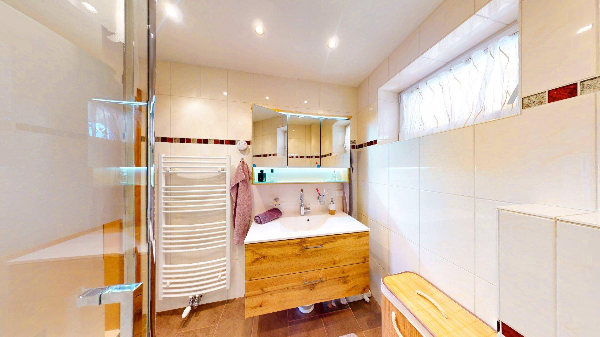 Helles Badezimmer mit Dusche, beheiztem Handtuchhalter und Holzwaschtisch.