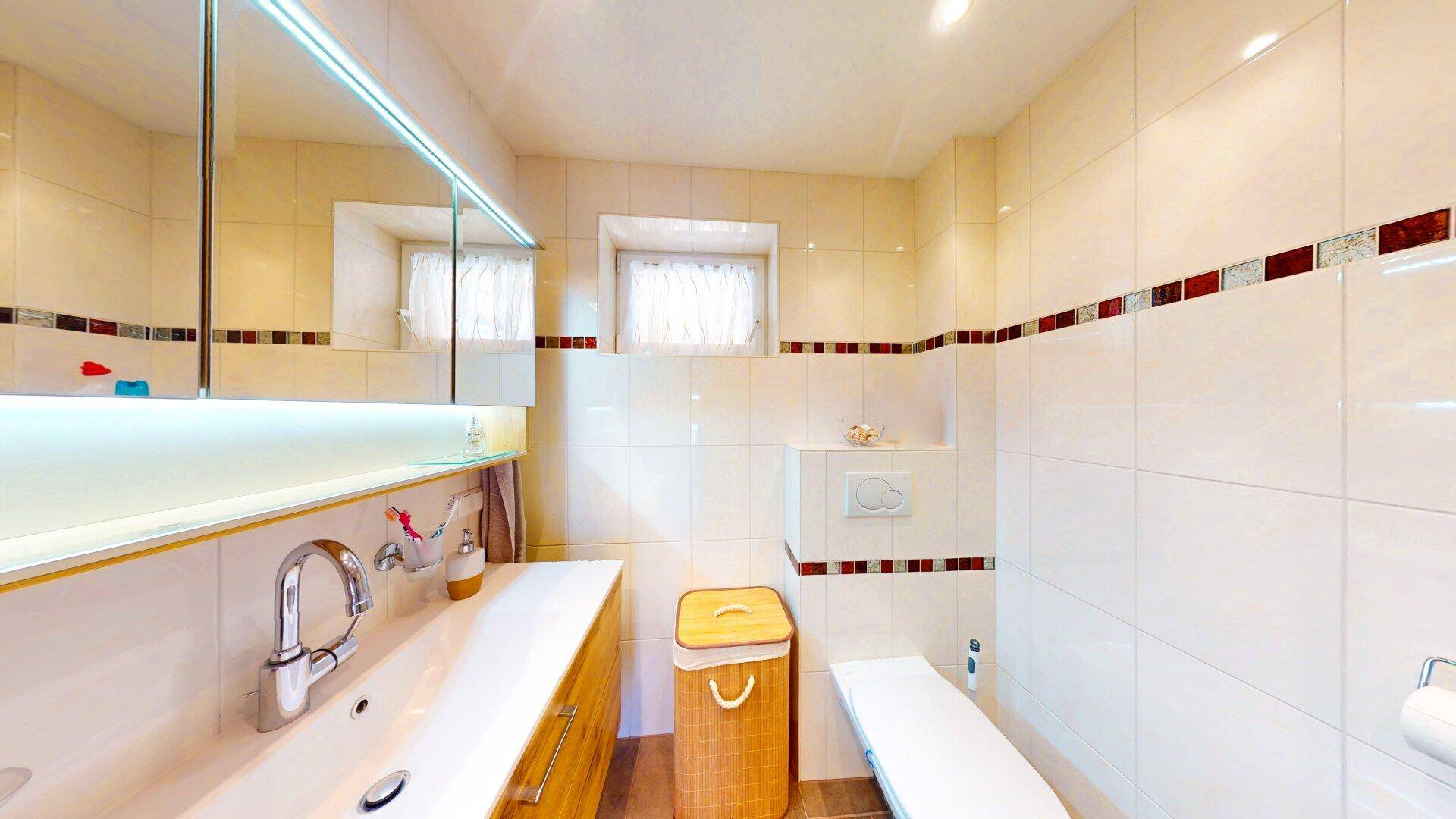 Modernes Badezimmer mit hellen Fliesen, Einzelwaschbecken und Spiegelschrank.