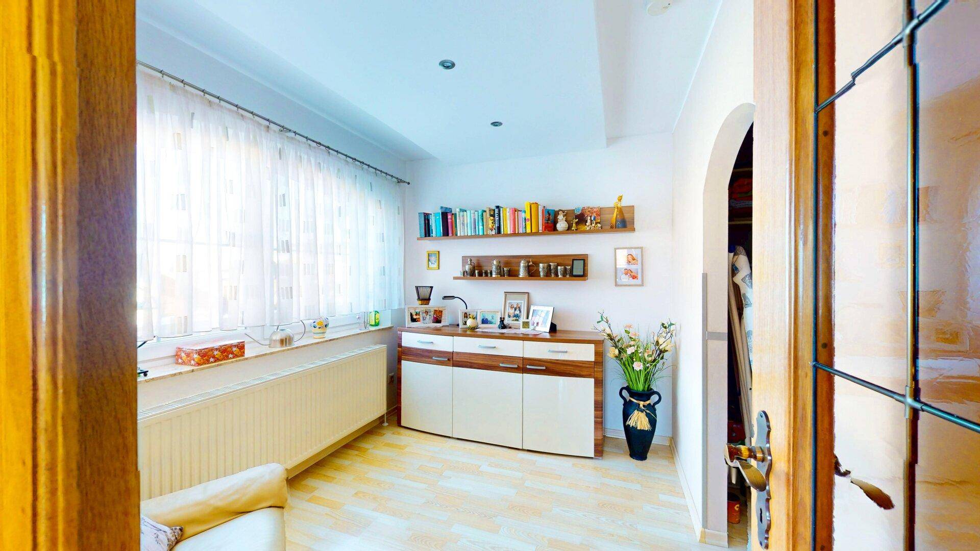 Helles Zimmer mit Laminatboden, Bücherregalen und großem Fenster, ideal als Büro.