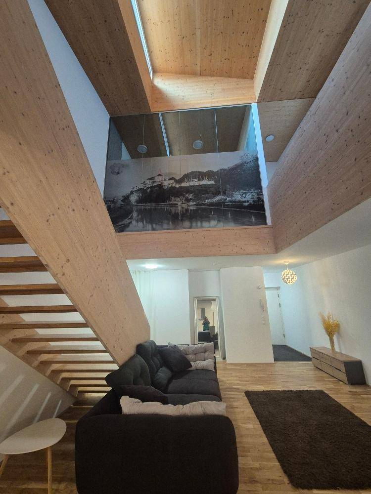 Geräumiges Wohnzimmer mit hoher Holzdecke, bequemer Couch und offener Holztreppe.