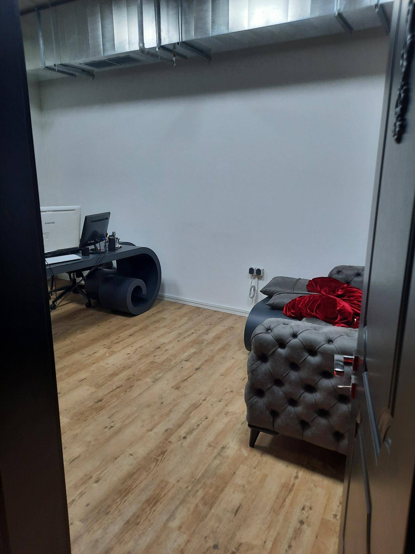 Ein schlichtes Büro mit einem modernen Schreibtisch, einem grauen Sofa und hellem Holzboden.