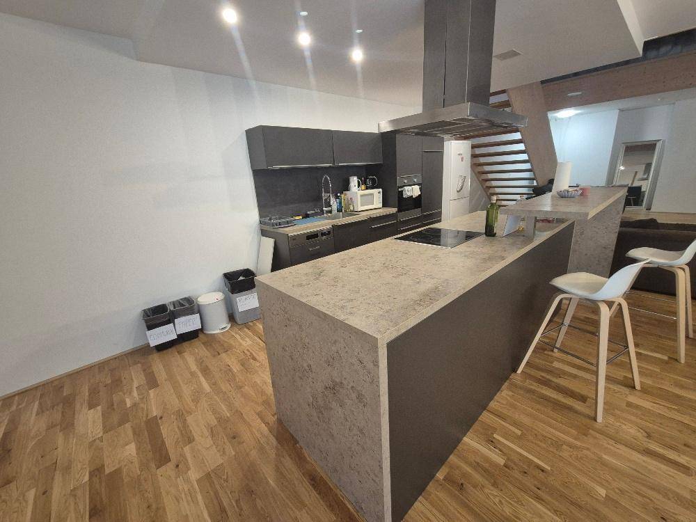 Moderne Küche mit Kücheninsel, dunklen Schränken und hochwertigem Holzfußboden.