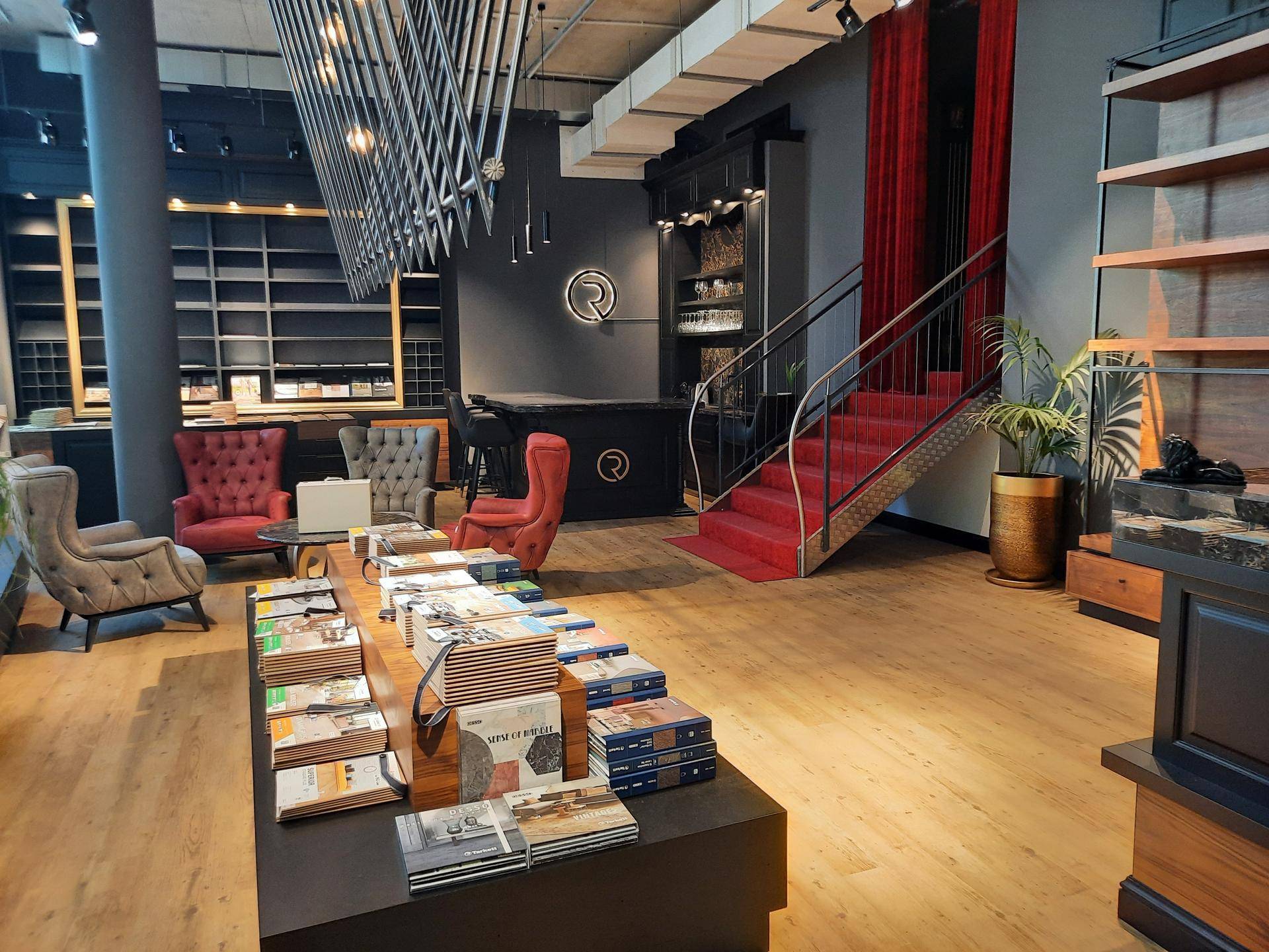 Ein geräumiger Showroom mit Holzboden, Ausstellungsflächen, einer Treppe mit rotem Teppich und hohen Decken.