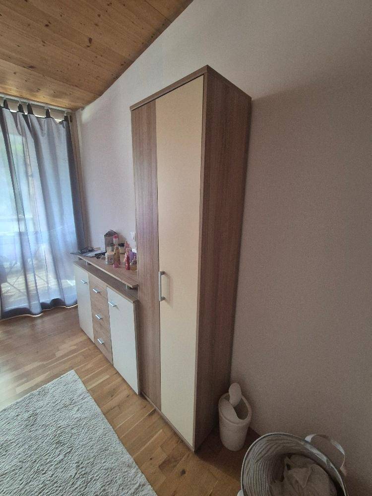 Gemütliches Schlafzimmer mit Holzfußboden, Kleiderschrank und Vorhängen am Fenster.
