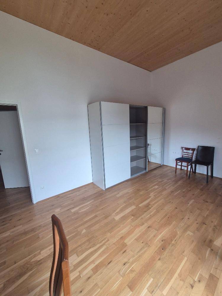 Helles Zimmer mit Holzfußboden, weißem Kleiderschrank und schlichter Einrichtung.