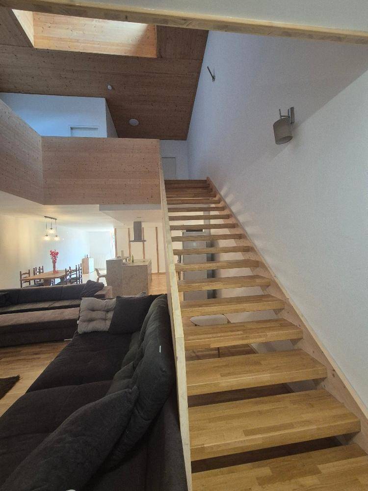 Offener Wohnbereich mit Holztreppe, bequemer Couch und Blick in den Essbereich.