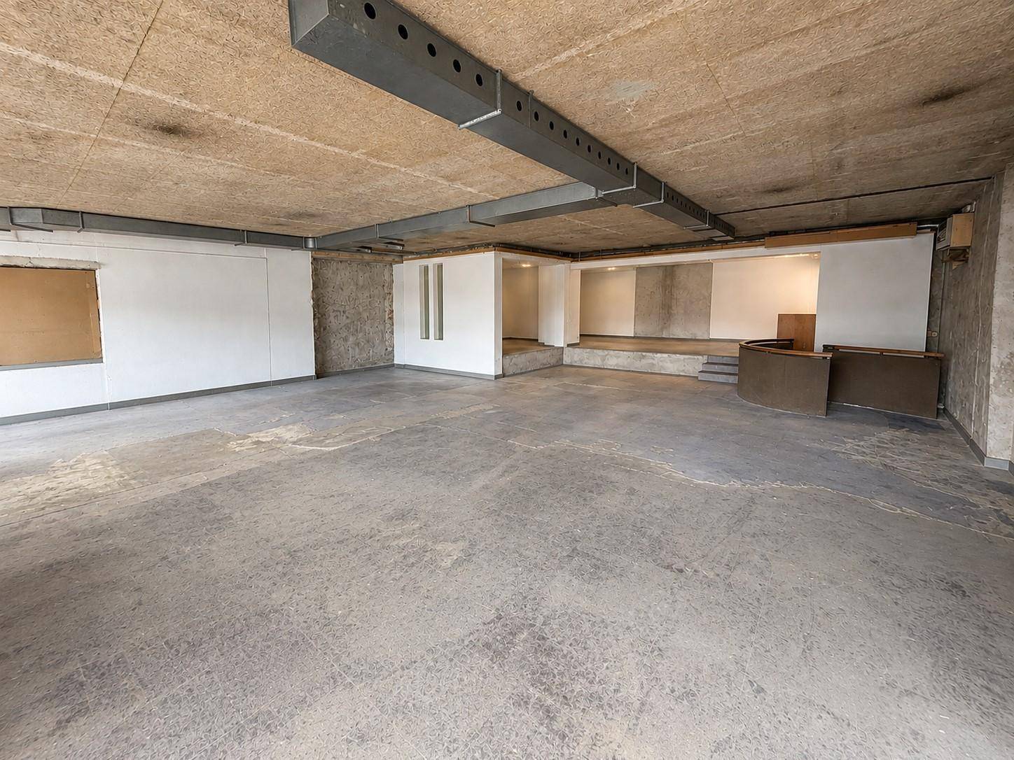 Großer, leerer Gewerberaum mit Sichtbetondecke, freiliegenden Metallträgern und Betonboden.