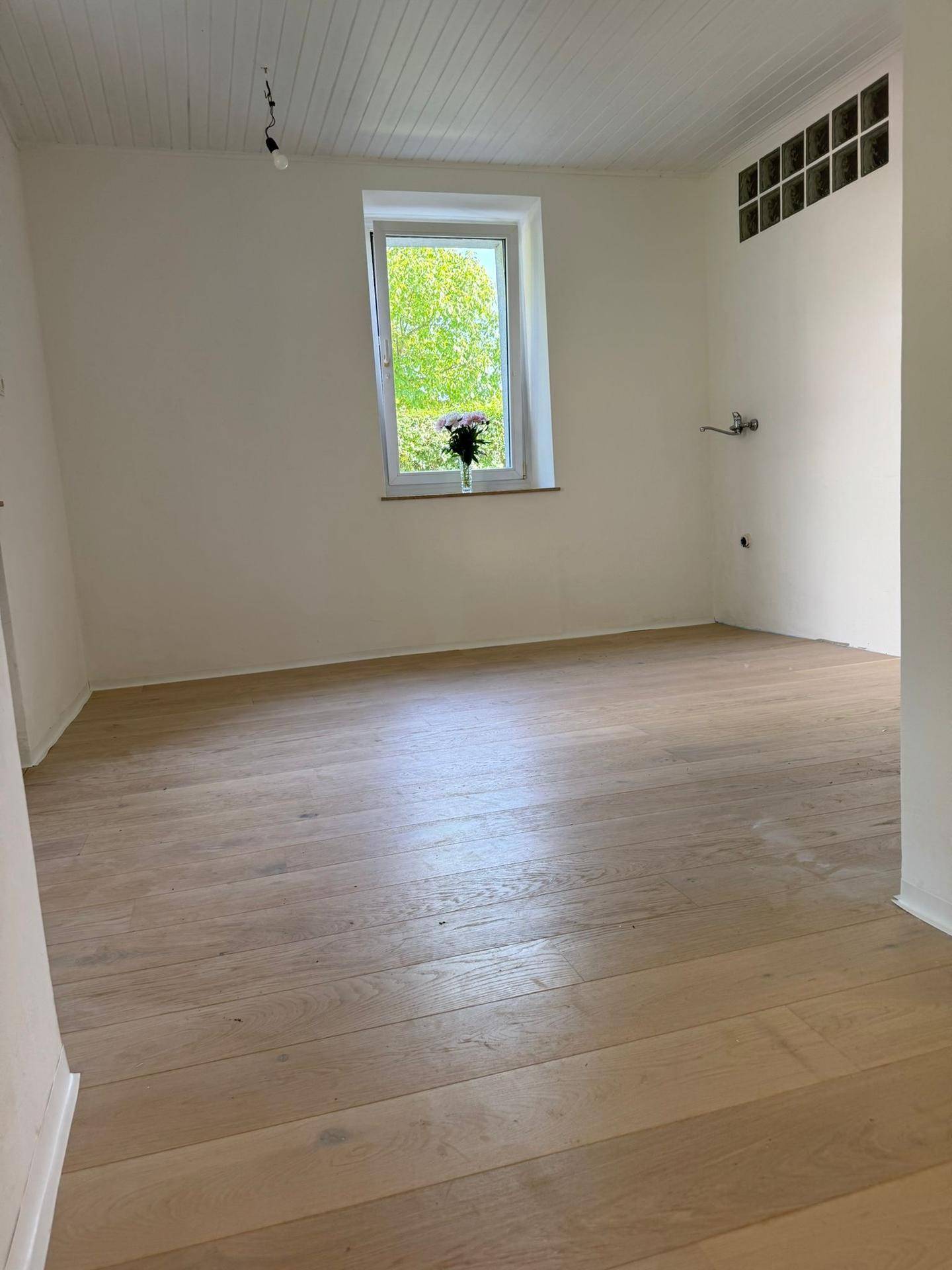 Heller Raum mit Holzboden, Fenster und einer Holzpaneeldecke, bereit für die Einrichtung.