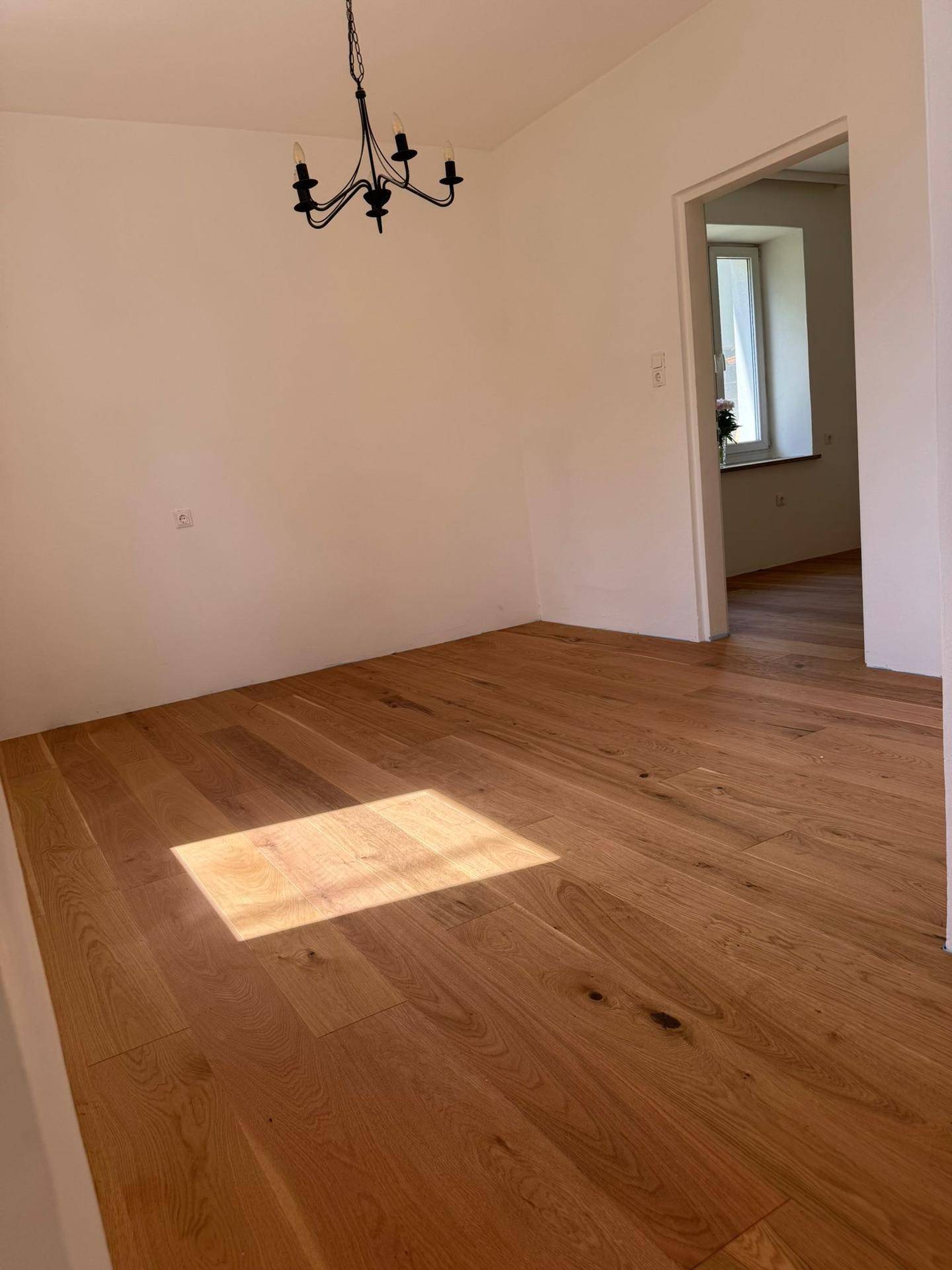 Renovierter Raum mit neuem Holzparkettboden und einer klassischen Deckenleuchte.