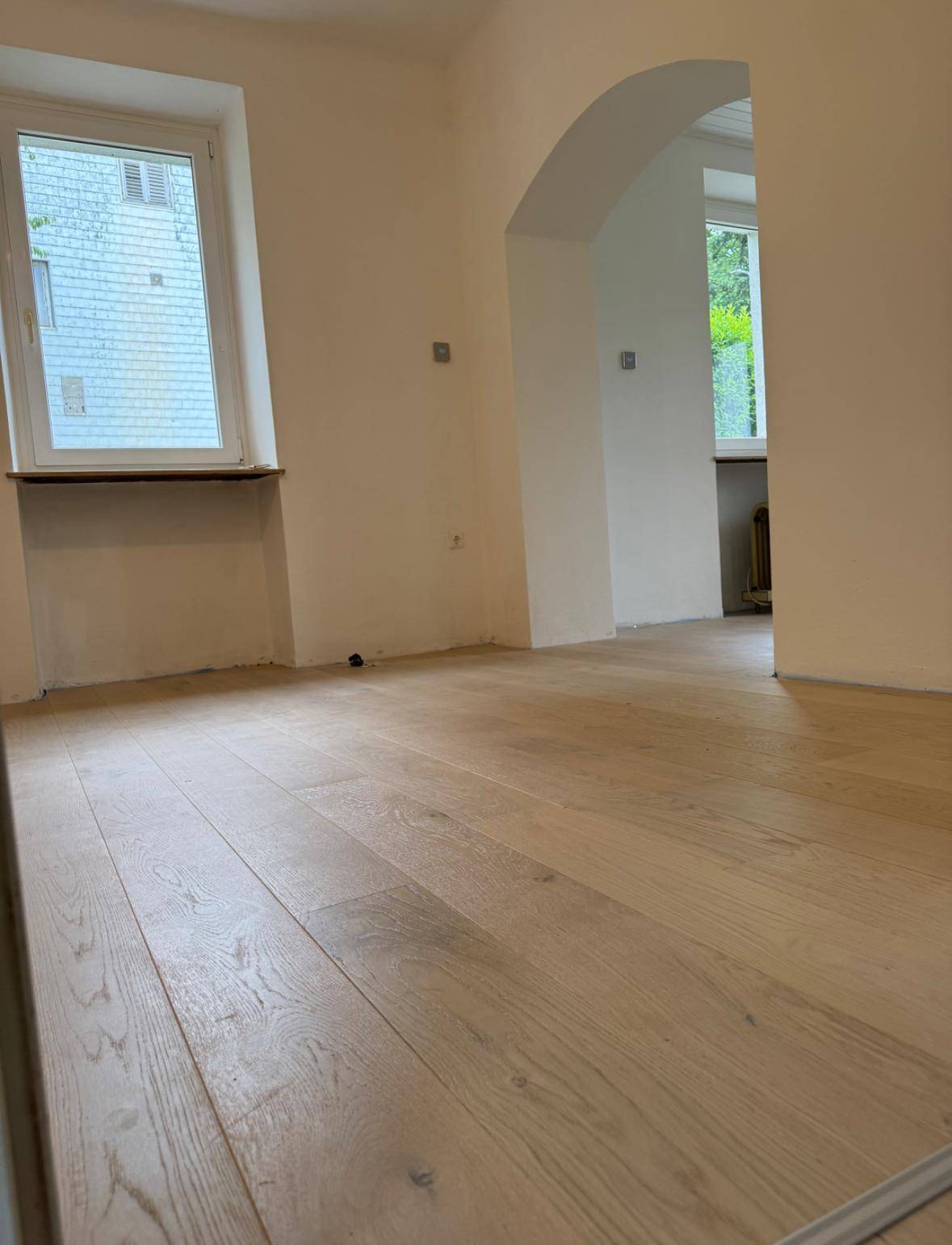 Heller, leerer Raum mit neuem Holzboden und einem Bogen, der zu einem weiteren Bereich führt.