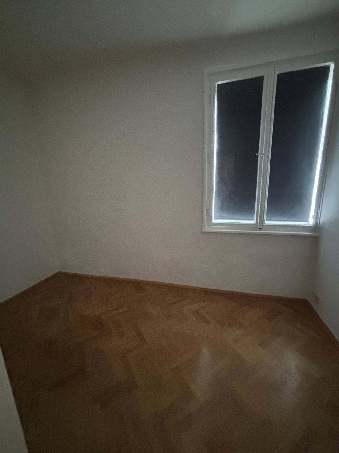 Leeres Zimmer mit Fischgrätparkett und einem Fenster, das für Tageslicht sorgt.